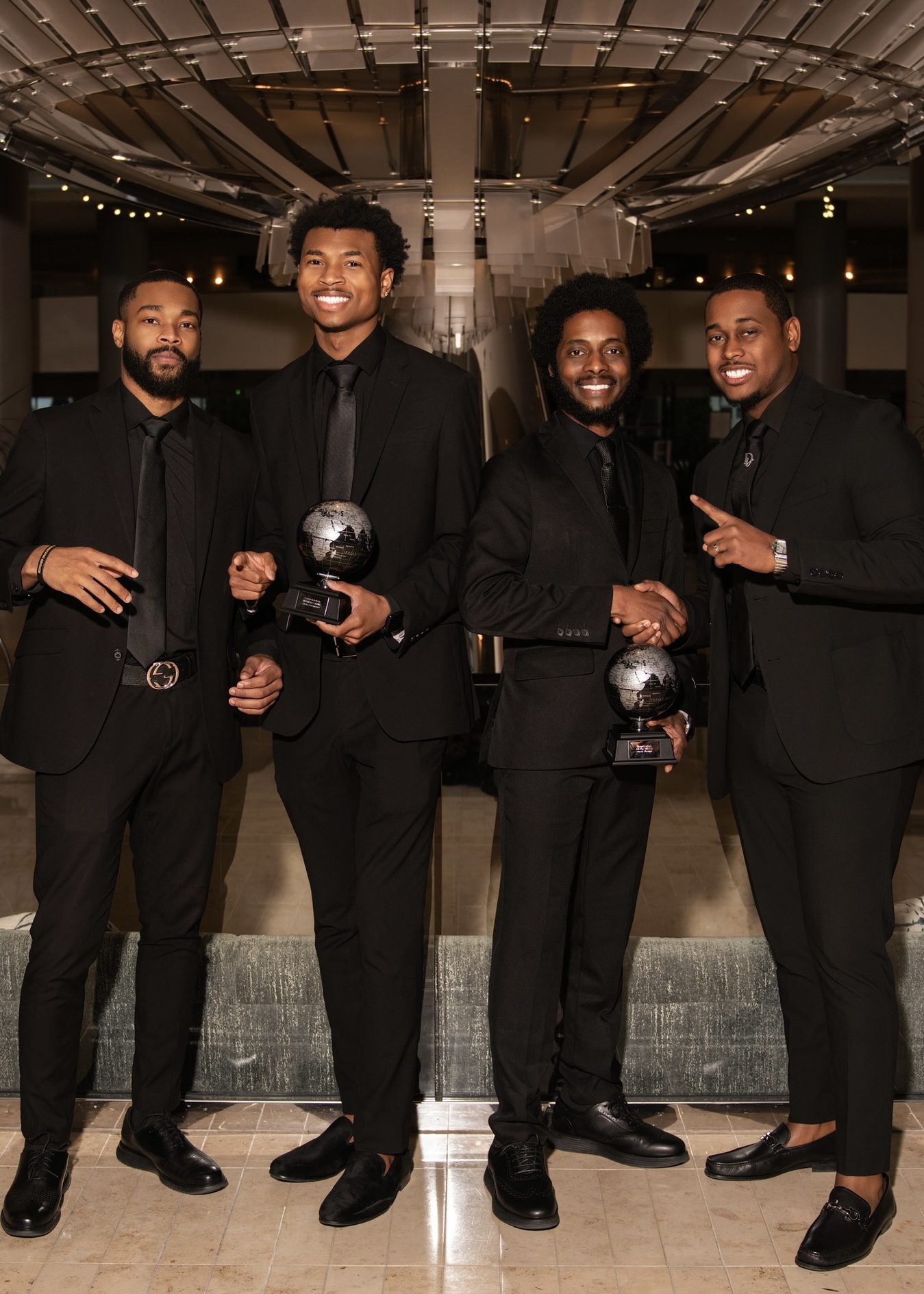 Four team members in formal black attire celebrating with globe achievement awards at a gala event
